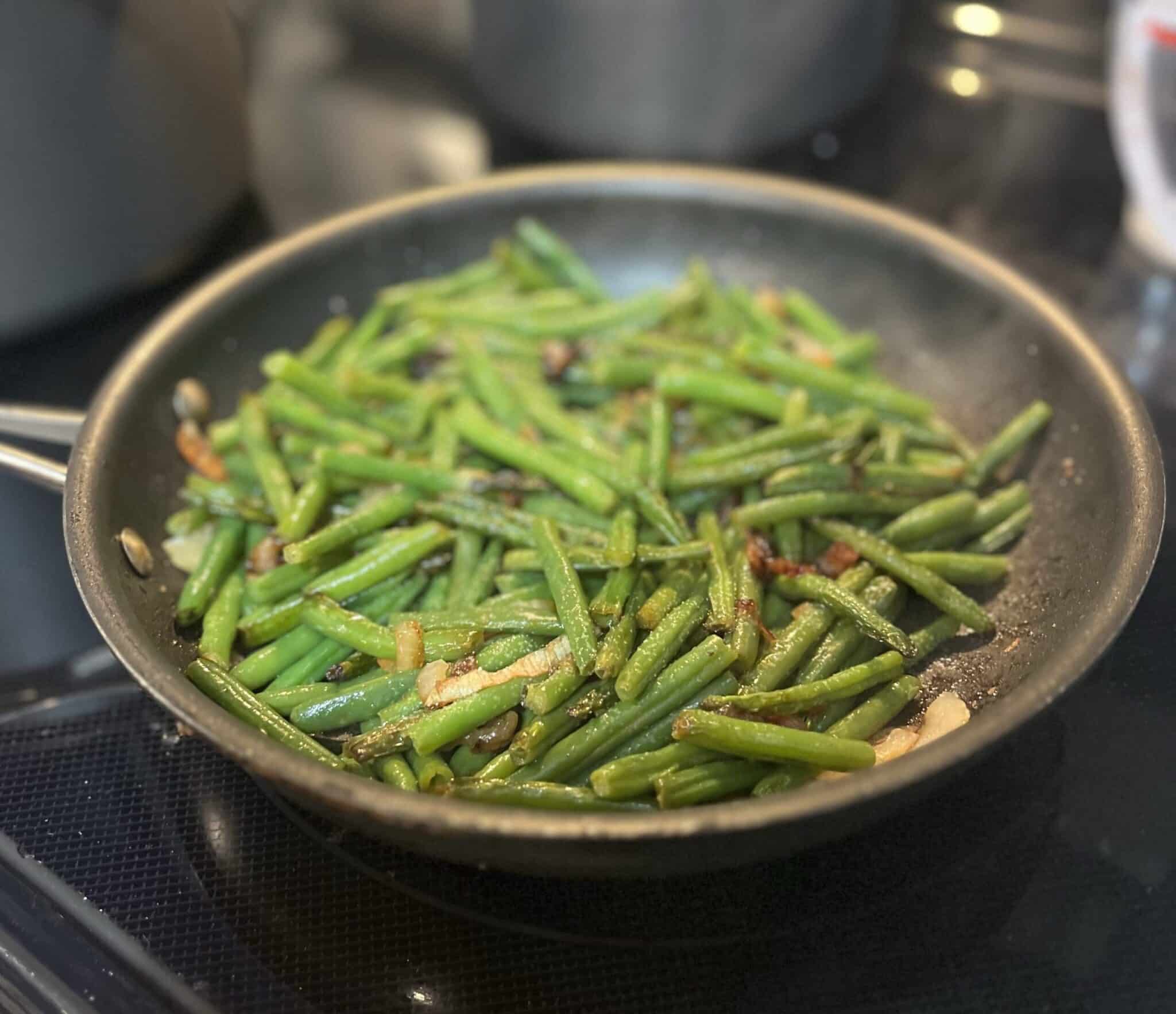 sauteed onions with fresh cooked green beans in a skillet pan