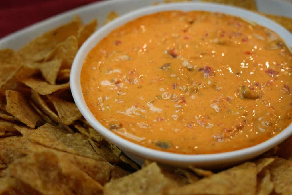 Chili cheese dip in a white bowl with tortilla chips surrounding the bowl