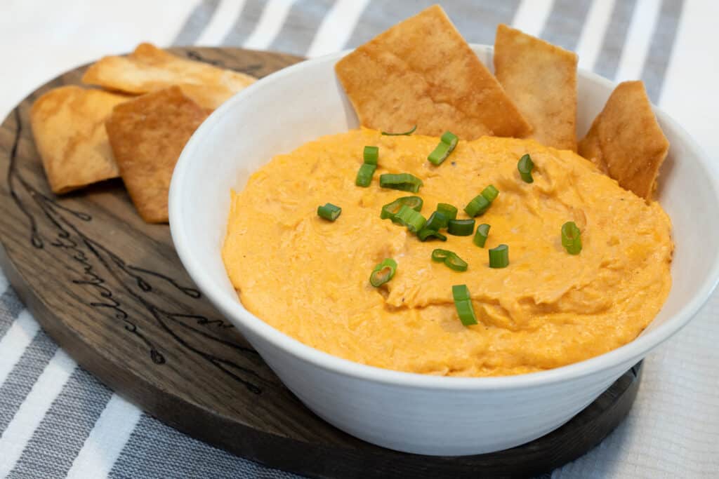 buffalo chicken dip in a white bowl garnished with chives pita chips for serving.