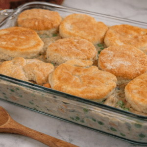 biscuit chicken pot pie in a 9x13 glass baking dish and wooden spoon sitting on the side