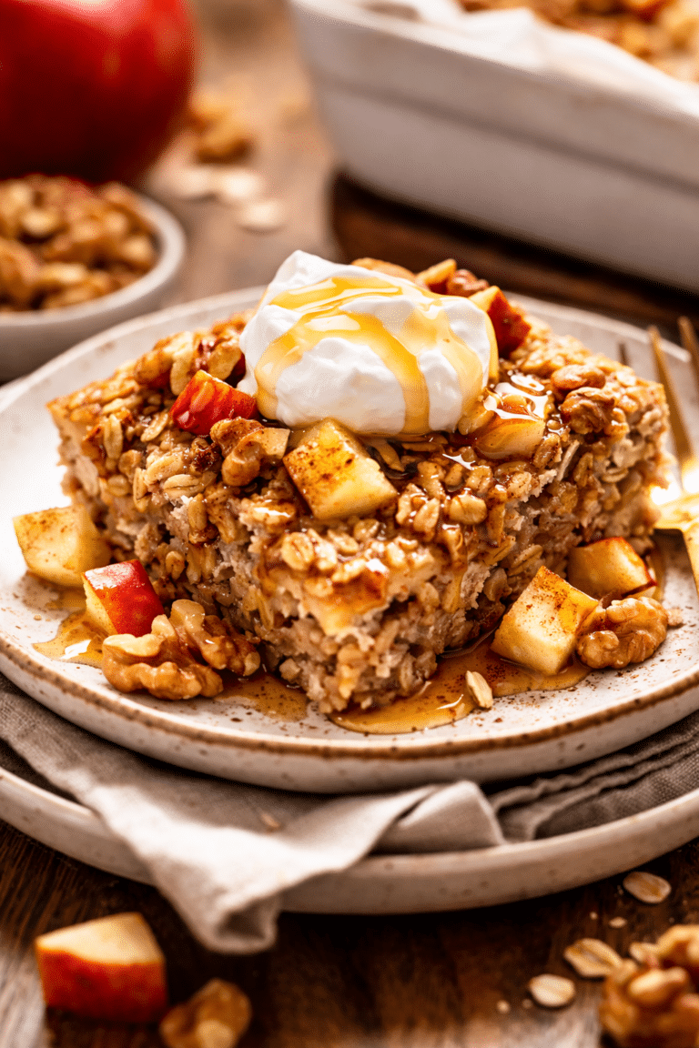 Apple and Walnut Baked Oatmeal sitting on a plate with a dollop of greek yogurt and maple syrup drizzle
