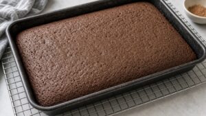 Baked chocolate cake in a 9x13 pan cooling on a stainless steel rack for Better Than Sex Cake
