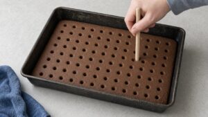 Poking holes in cooled chocolate cake with a wooden dowel for Better Than Sex Cake