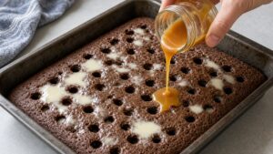 Pouring sweetened condensed milk and caramel over the cooled chocolate poke cake for Better Than Sex Cake