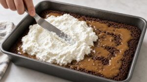 Spreading whipped topping over chilled Better Than Sex Cake with an offset spatula