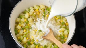 Stirring whole milk and corn into creamy corn chowder with a wooden spoon