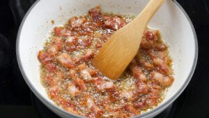 Strips of bacon cooking in a white enameled Dutch oven for creamy corn chowder