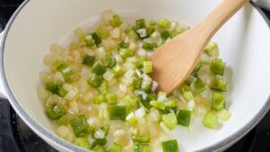Diced yellow onion, celery and green bell pepper sautéing in bacon grease in a white Dutch oven