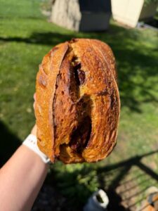 Hand holding a pumpkin cinnamon swirl sourdough loaf outdoors with the swirl showing through the scored crust